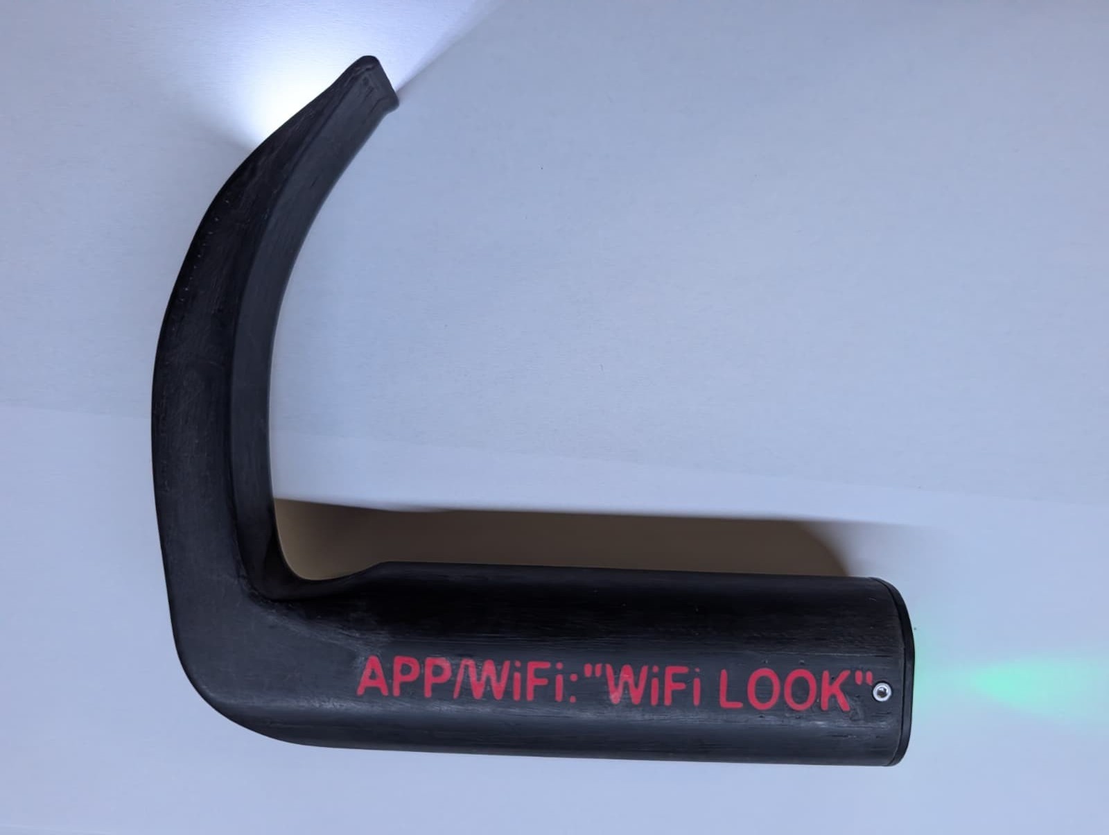 Hyperanguliertes Laryngoskop von der Seite mit der roten Aufschrift APP/WiFi: &ldquo;WiFi LOOK&rdquo; auf dem Griff, an der Spatelspitze leuchtet die Kamerabeleuchtung
